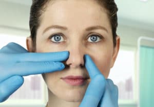 surgeon's hands on woman's nose in preparation for rhinoplasty surgery